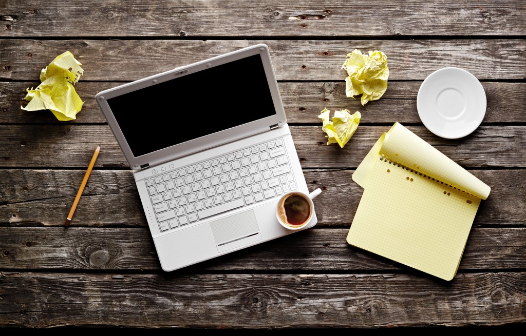 Laptop with crumpled paper, blank notepad and pencil on old wood