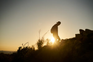 bearded hiker with backpack walking up hill during sunset
